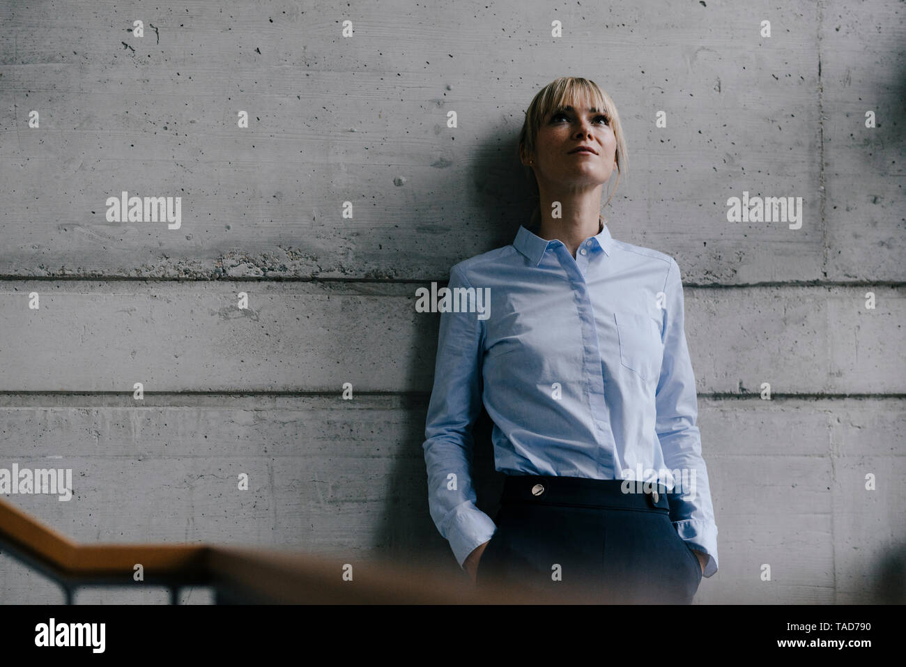Businesswoman leaning on concrete wall, looking up Stock Photo