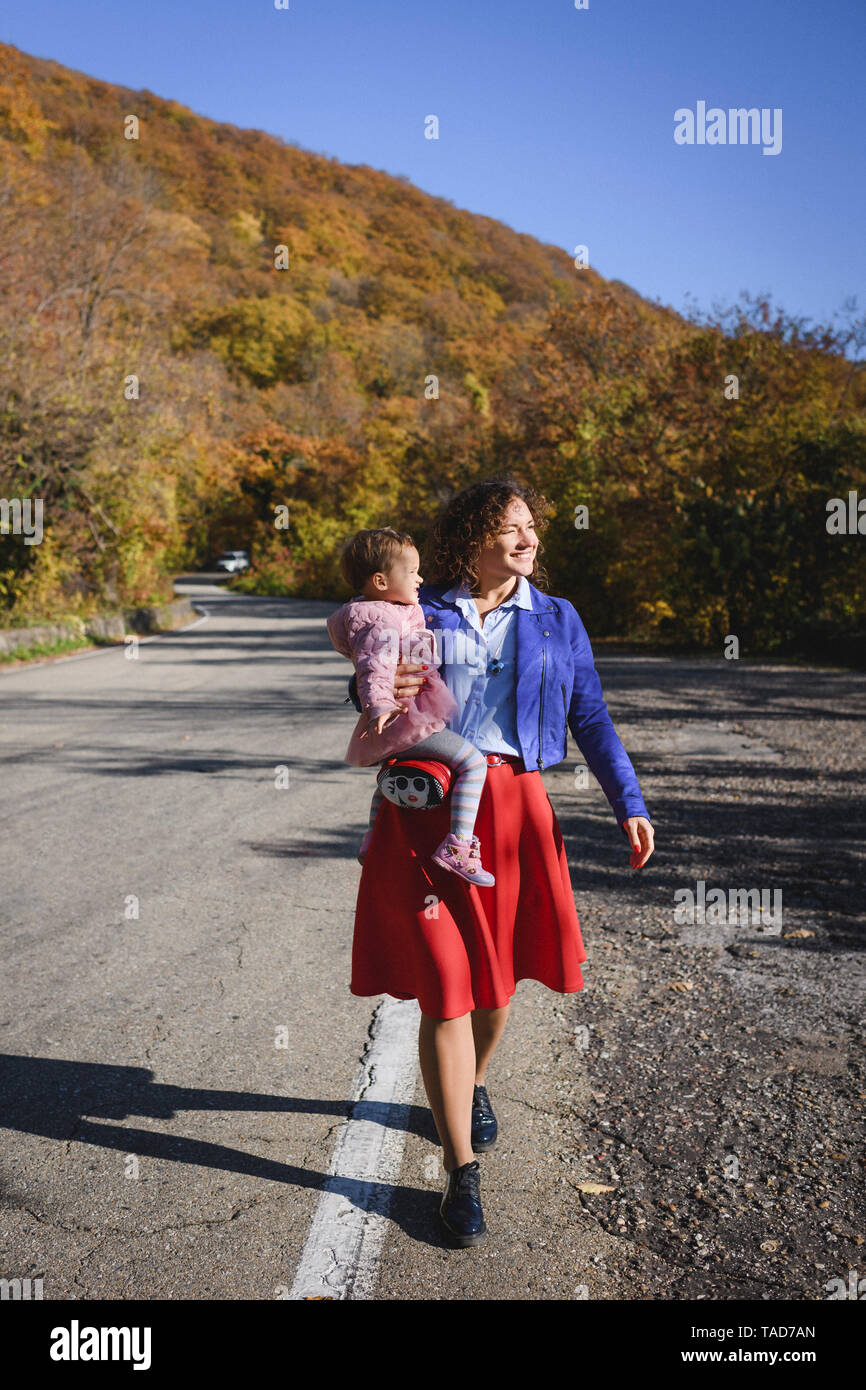 Happy mother carrying her daughter on a country road Stock Photo