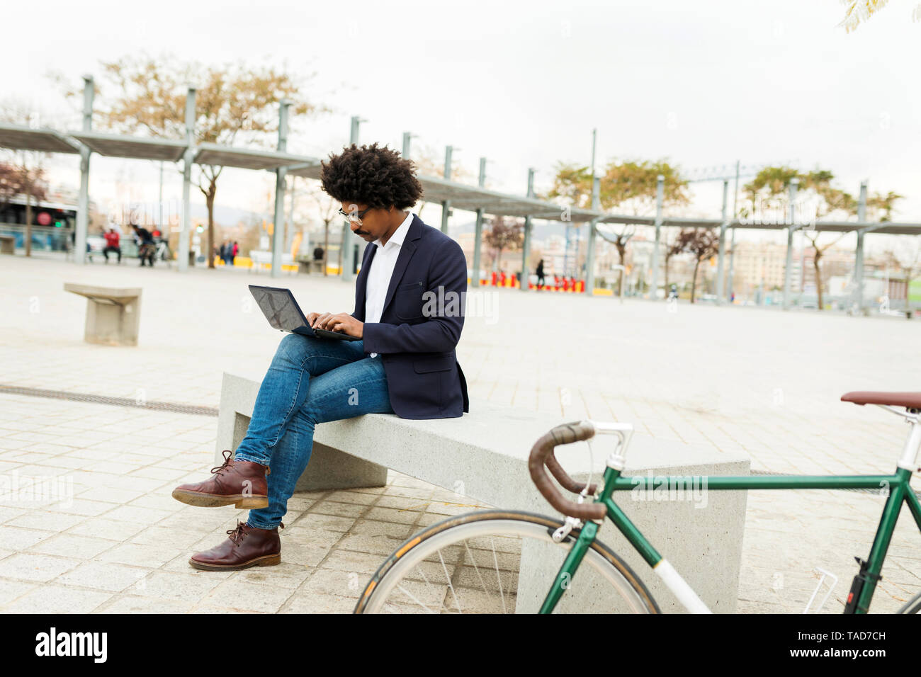 Spain, Barcelona, businessman with bicycle in the city sitting on bench using laptop Stock Photo