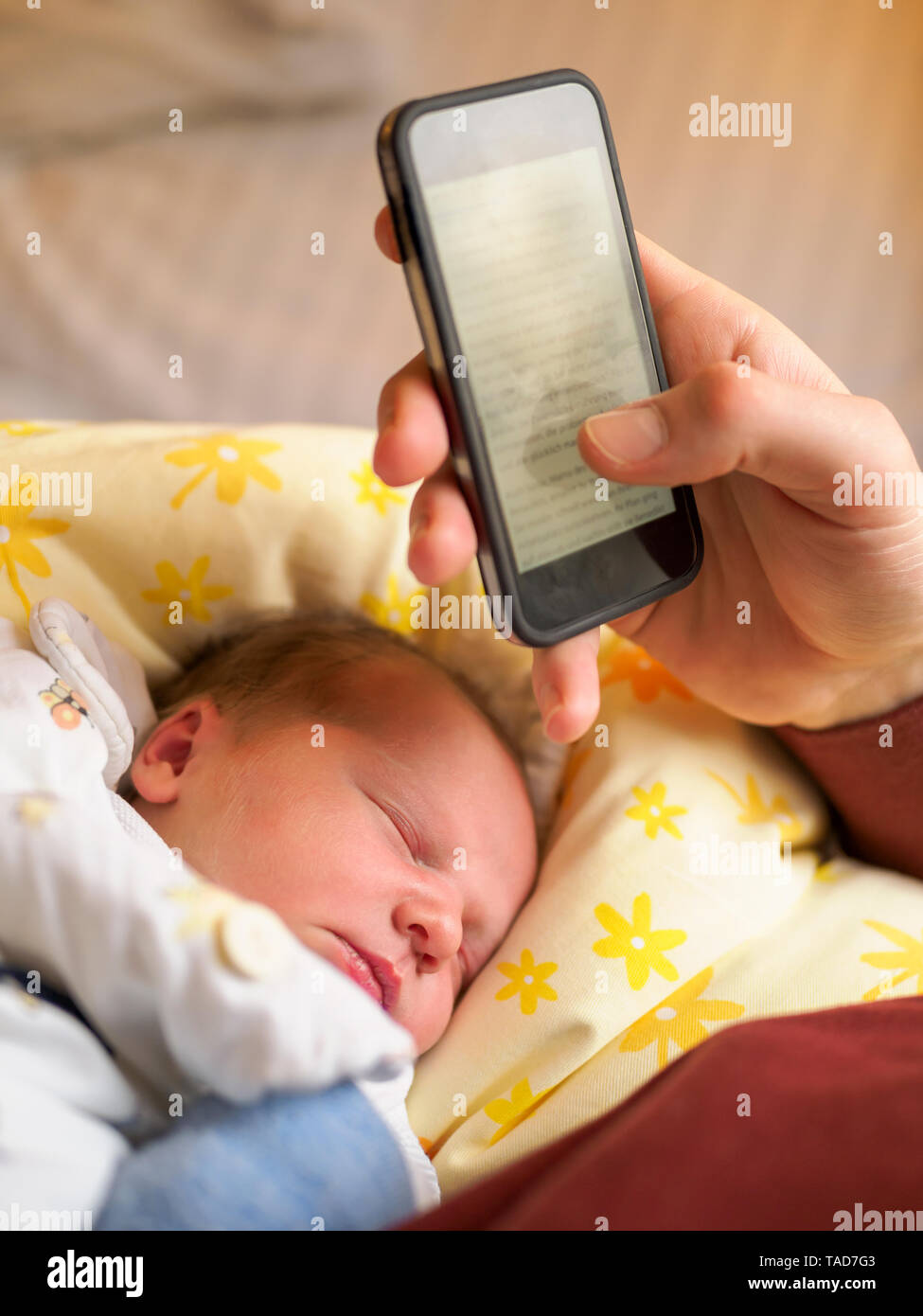 Father using smartphone, newborn girl sleeping Stock Photo