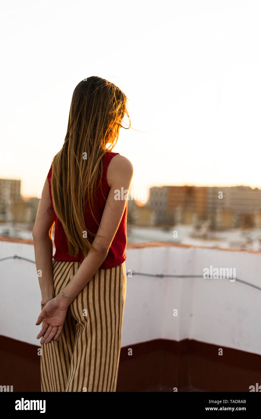 Rear view of teenage girl standing on roof terrace in the city at sunset Stock Photo