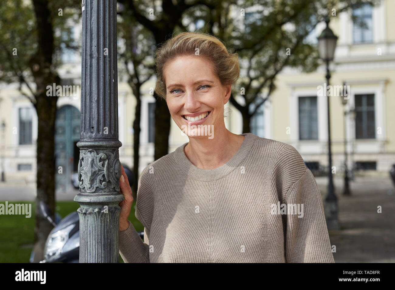 Portrait of smiling woman leaning against lamp post in the city Stock Photo