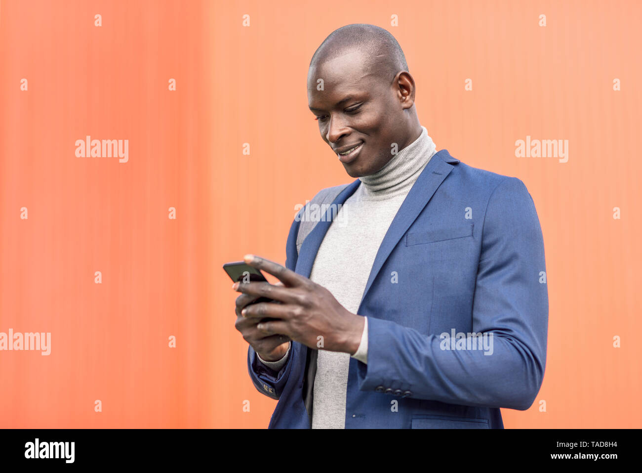 Smiling businessman standing in front of orange wall looking at ...