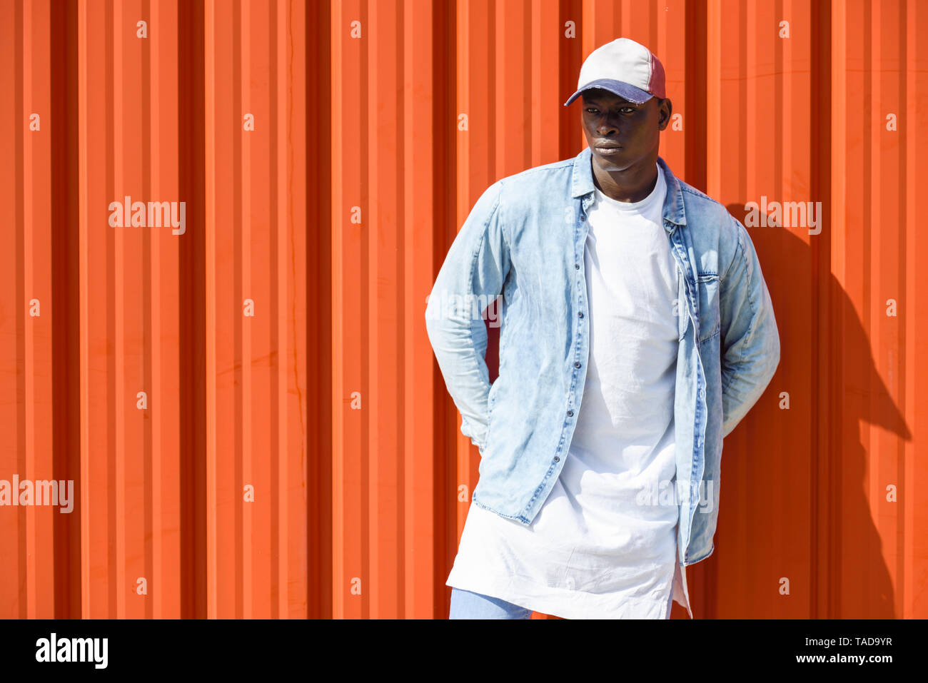 Man wearing casual denim clothes and cap standing in front of orange wall  Stock Photo - Alamy