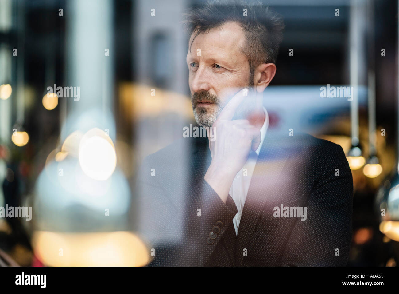 Portrait of pensive mature businessman behind window pane Stock Photo