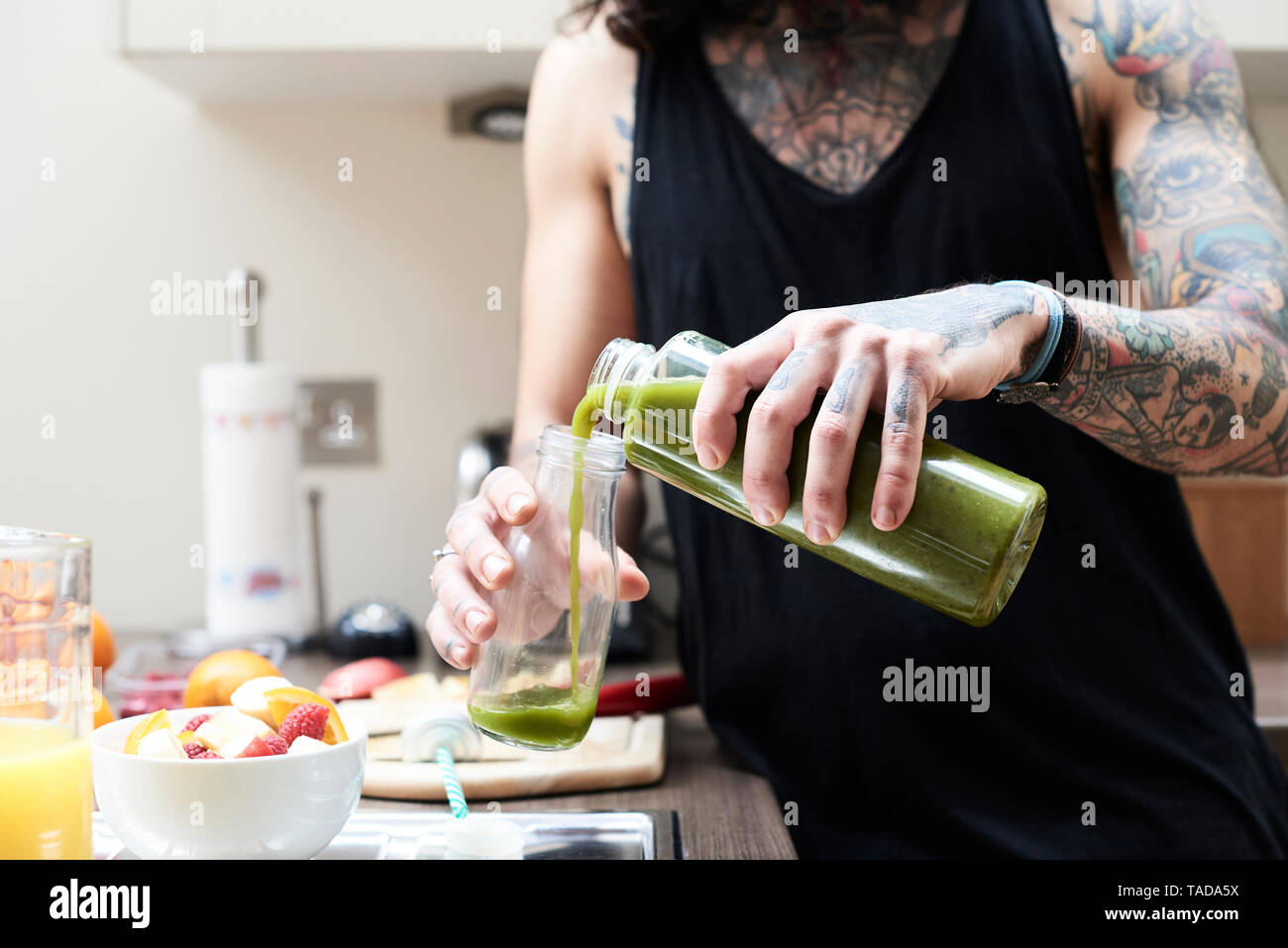 Tattooed young man pouring in healthy smoothie in kitchen Stock Photo