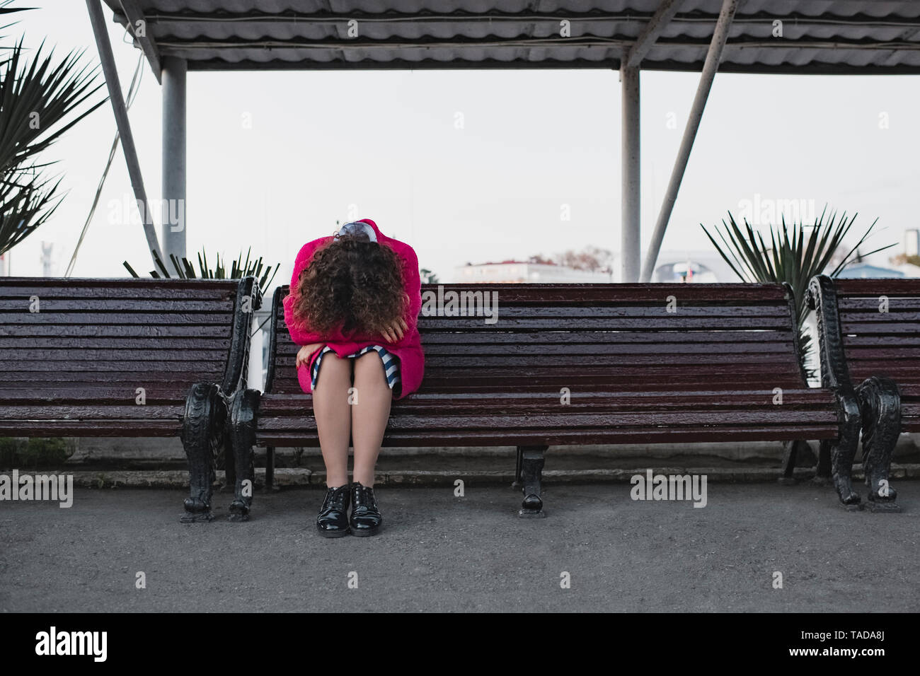 Depressed woman with curly hair sitting on a bench Stock Photo
