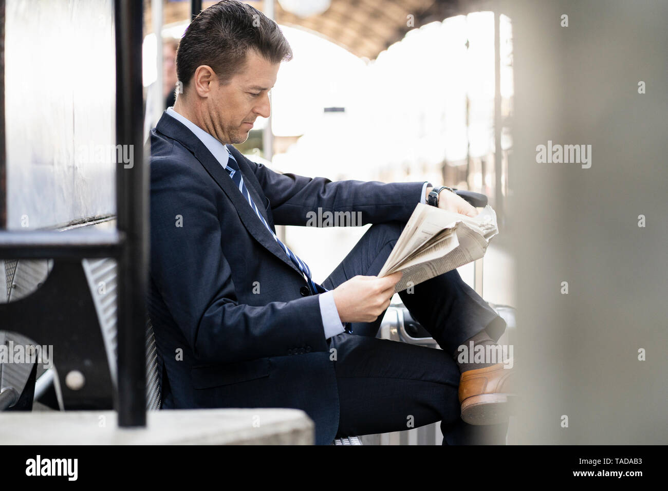 Businessman reading newspaper on station platform Stock Photo