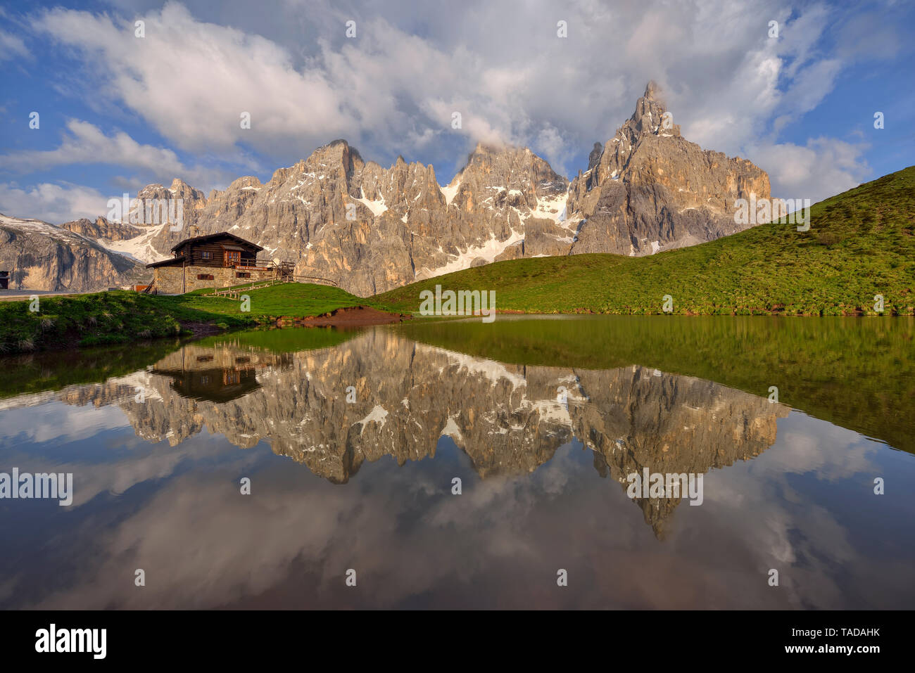 Italy, Trentino, Dolomites, Passo Rolle, Pale di San Martino range, Cimon della Pala with Baita Segantini reflecting in small lake in the evening Stock Photo