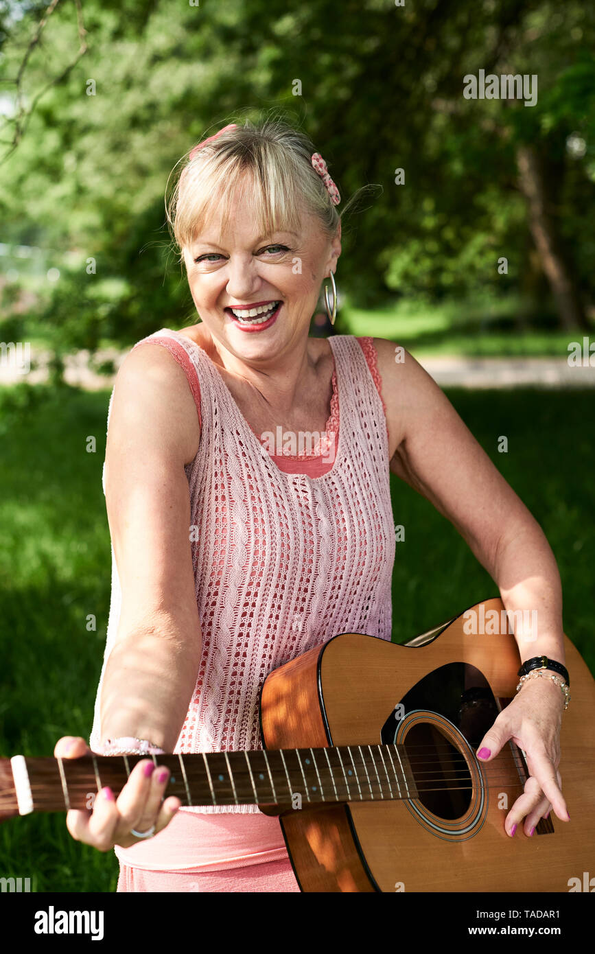 Portrait of happy senior woman playing guitar in park Stock Photo