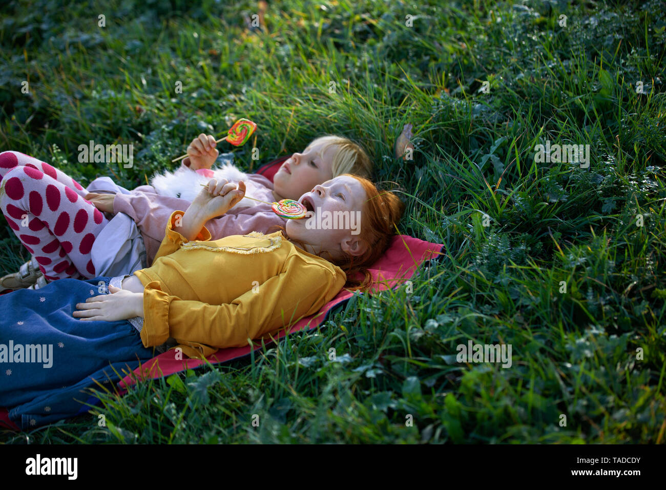 Two sisters lying in a field holding lollipops Stock Photo