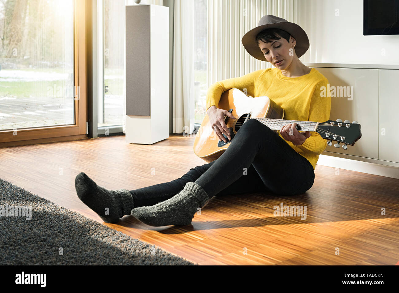 Woman sitting on the floor of living room playing guitar Stock Photo