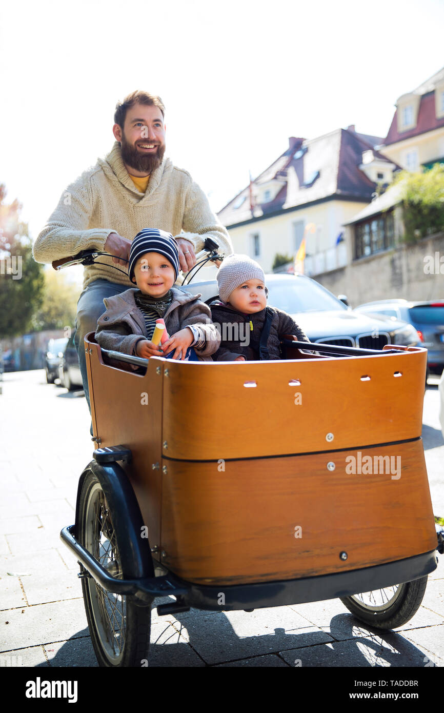 Happy father with two children riding cargo bike in the city Stock Photo