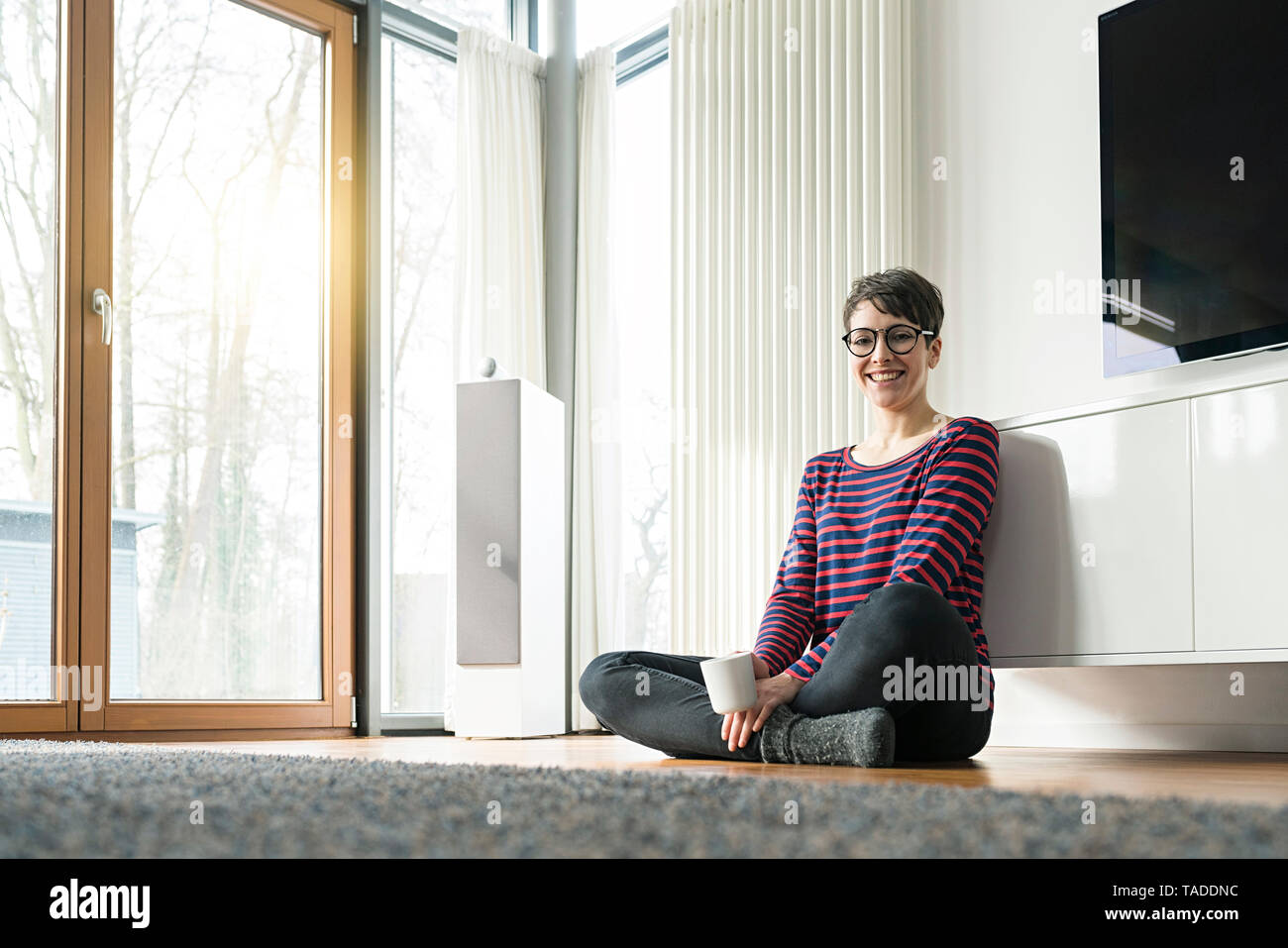 Portrait of laughing woman sitting on the floor of living room Stock Photo