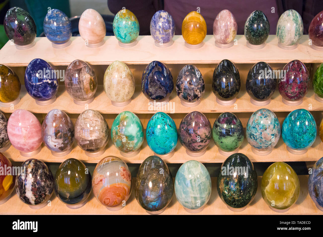 Different multicolored stone eggs arranged on a wooden rack at the mineral exhibition Stock Photo