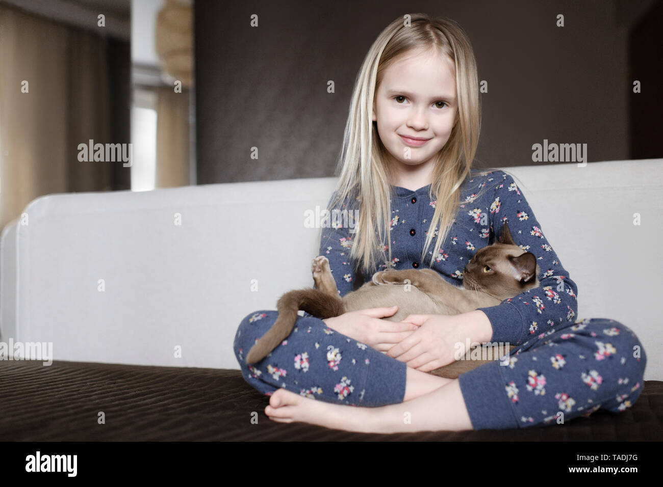Portrait of smiling little girl wearing pyjama with floral design holding cat in her arms Stock Photo