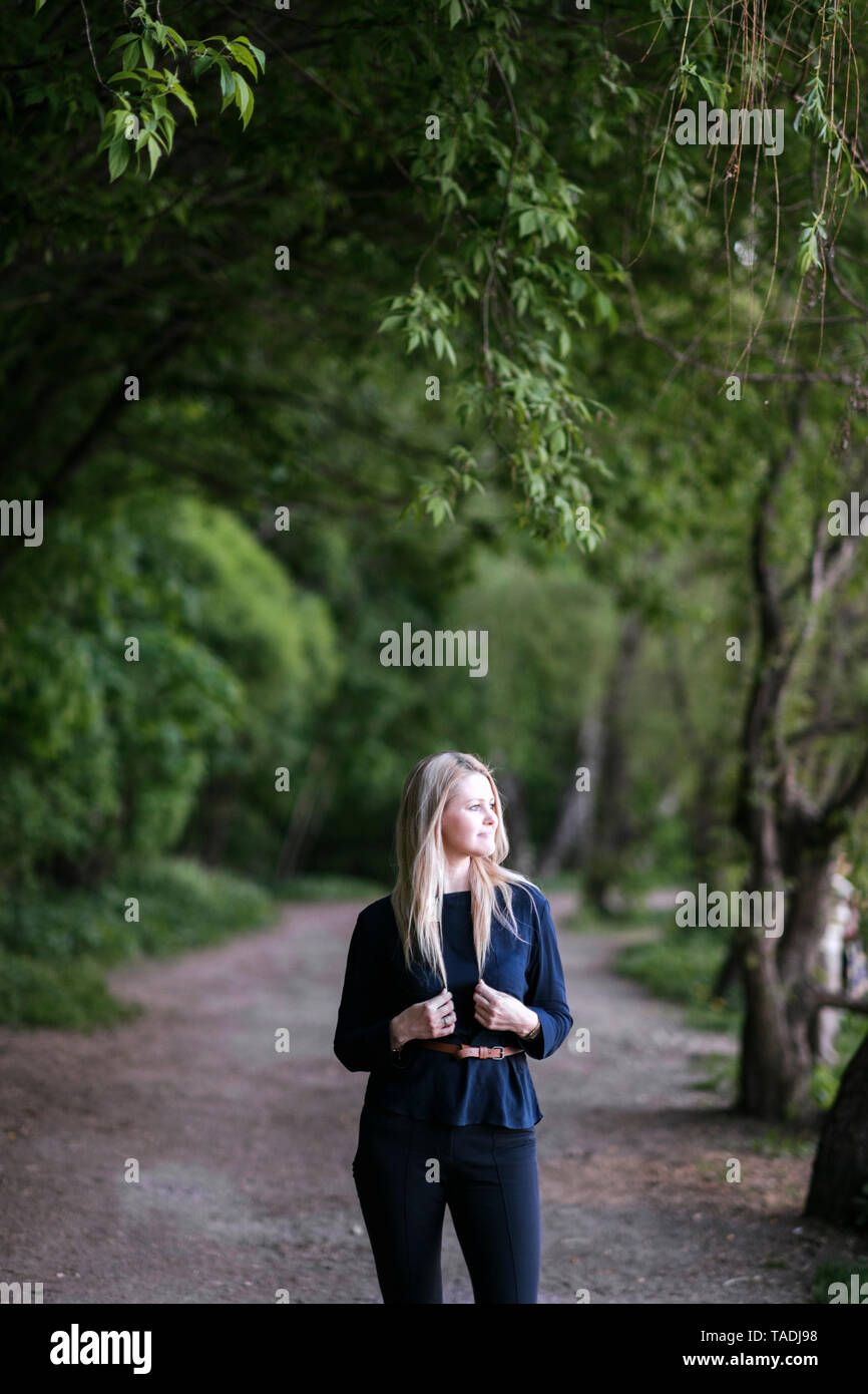 Blond woman standing on a path in park looking sideways Stock Photo