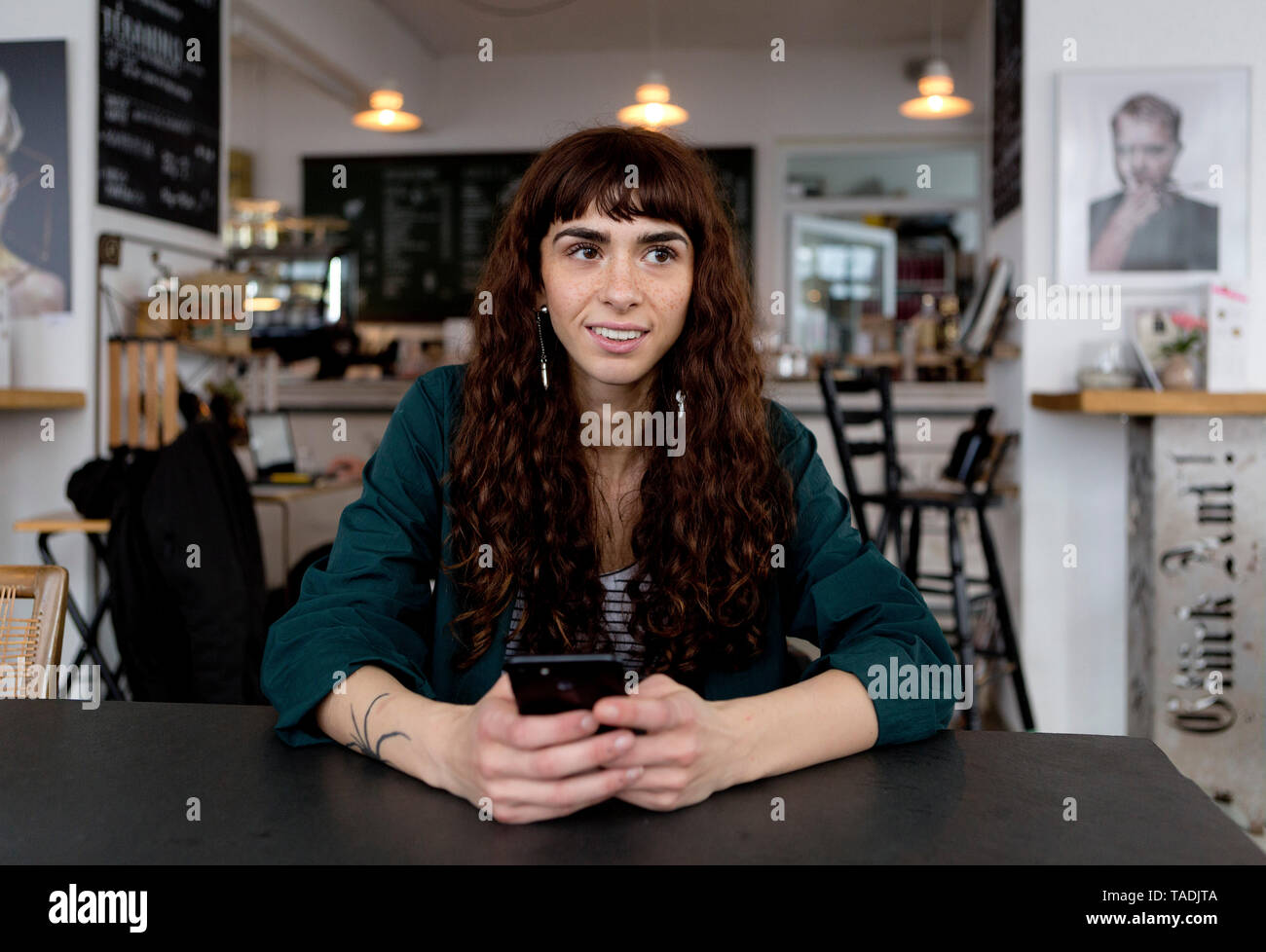 Smiling young woman with cell phone in a cafe looking around Stock Photo