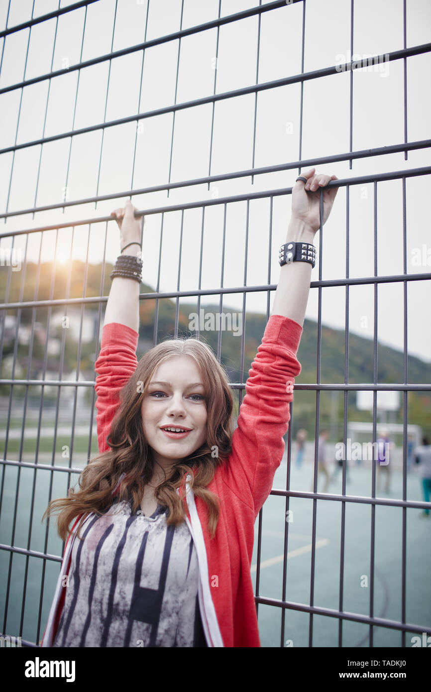 Portrait of a happy teenage girl at a fence at a sports field Stock Photo
