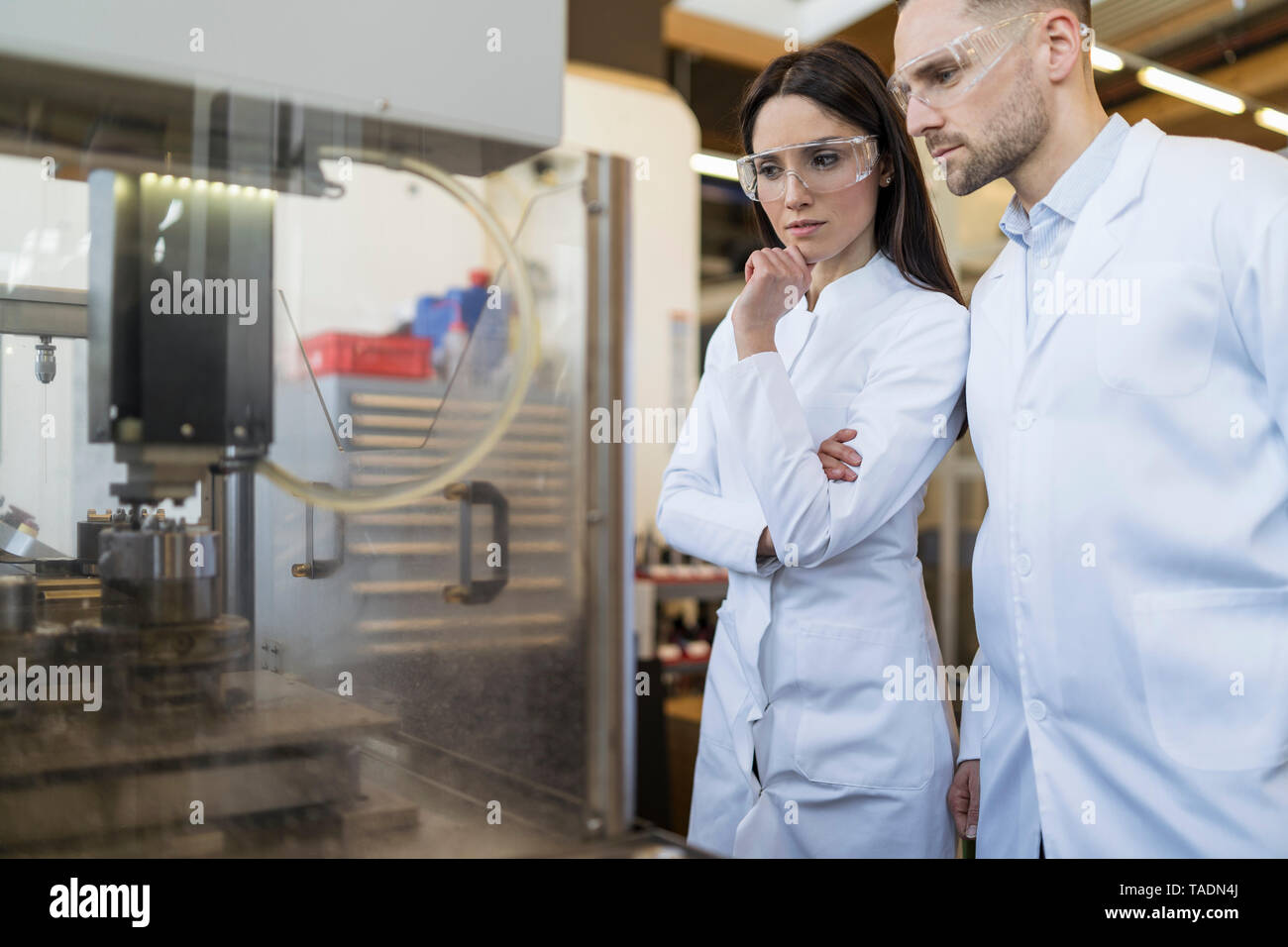 Colleagues wearing lab coats and safety goggles looking at machine in