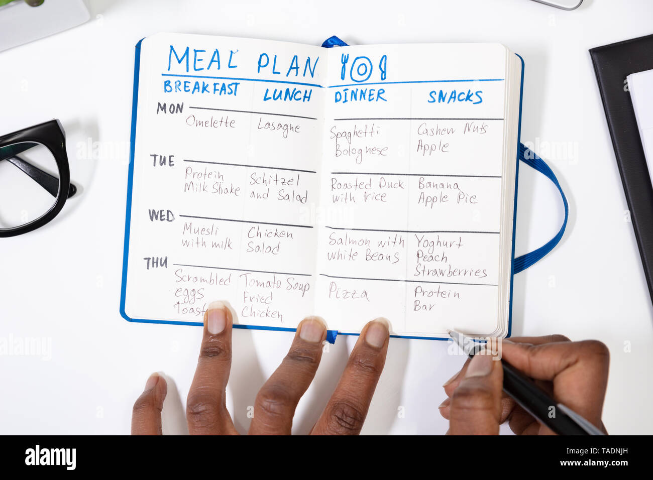 High Angle View Of A Person's Hand Filling Meal Plan On Notebook Stock Photo