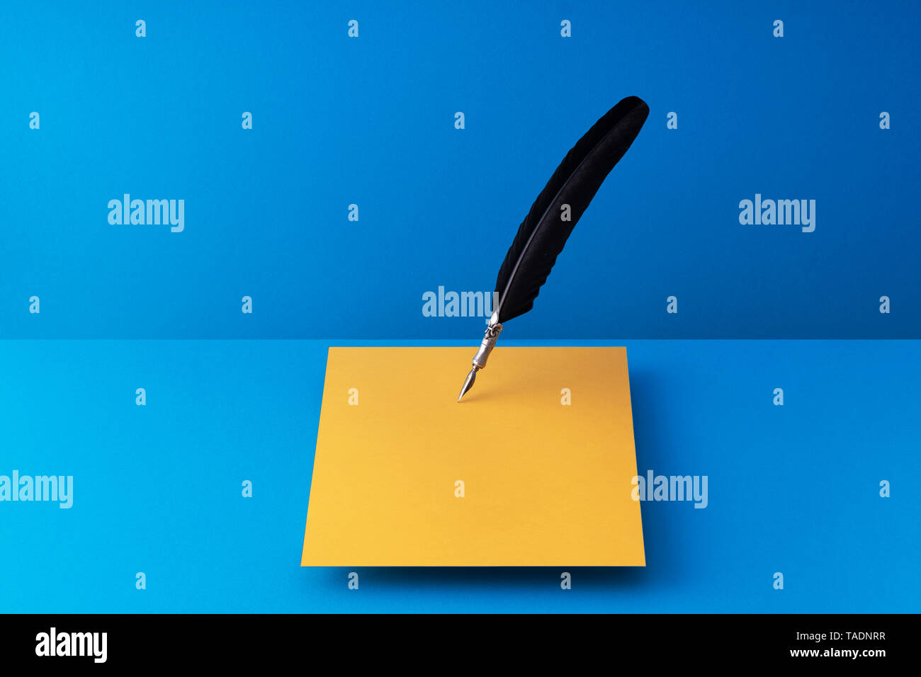 Quill pen writing on orange paper over blue background Stock Photo