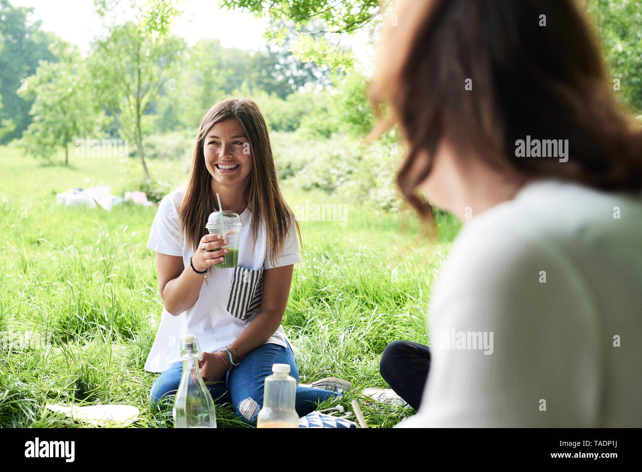 Happy young woman drinking juice with friends at a picnic in park Stock Photo