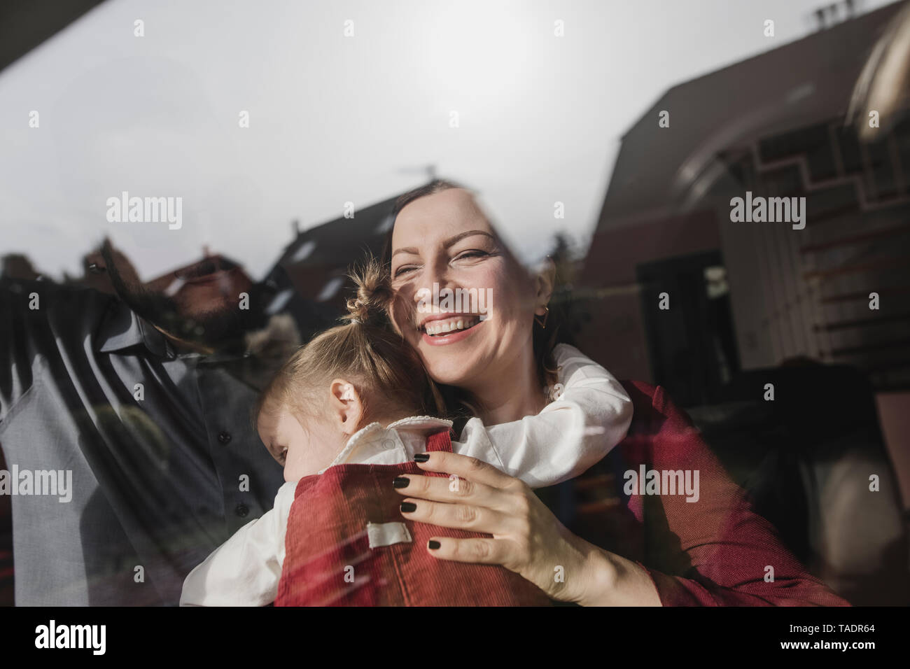 Happy mother embracing daughter behind windowpane Stock Photo
