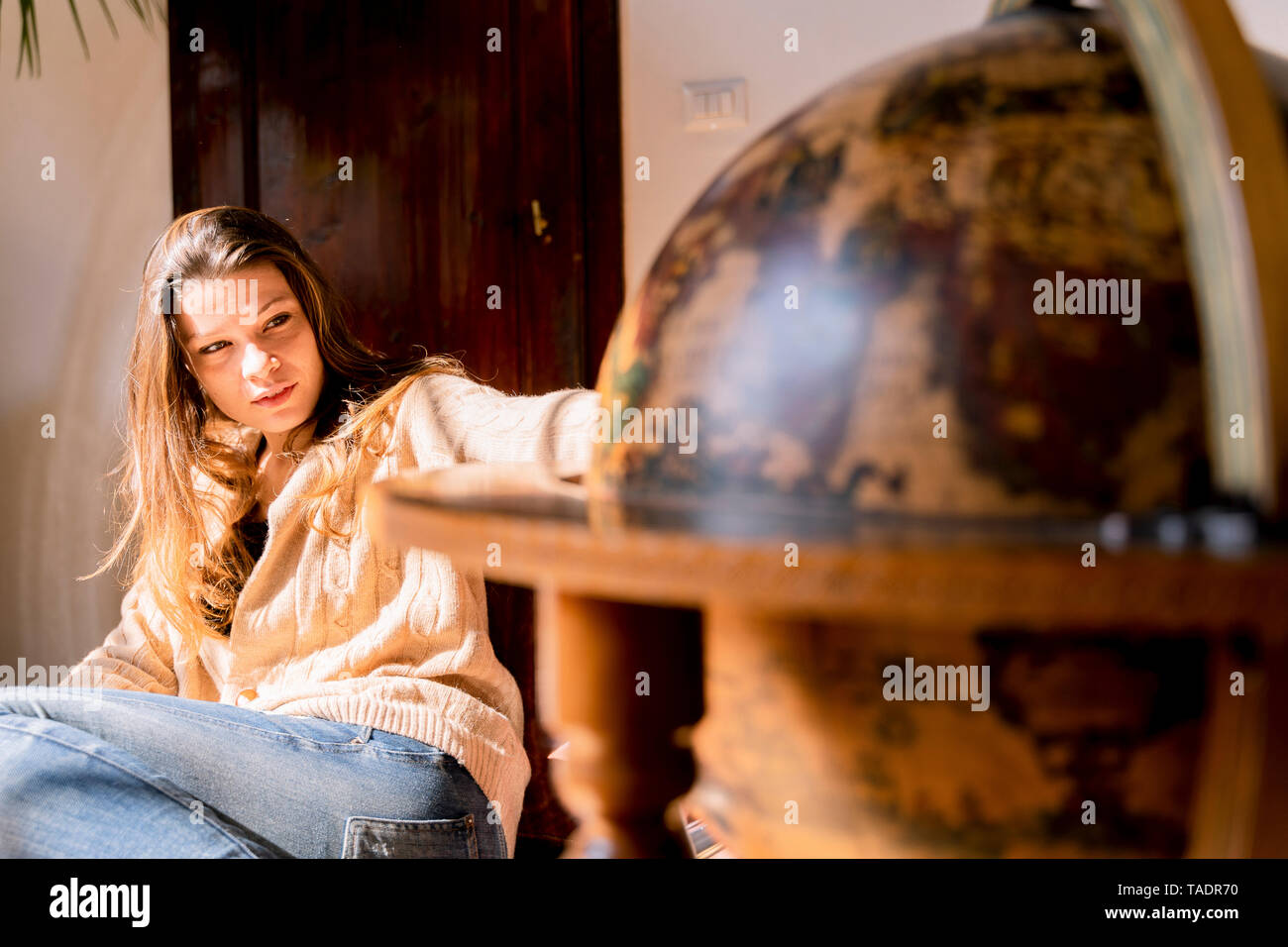 Young woman sitting by globe, looking for travel destinations Stock Photo