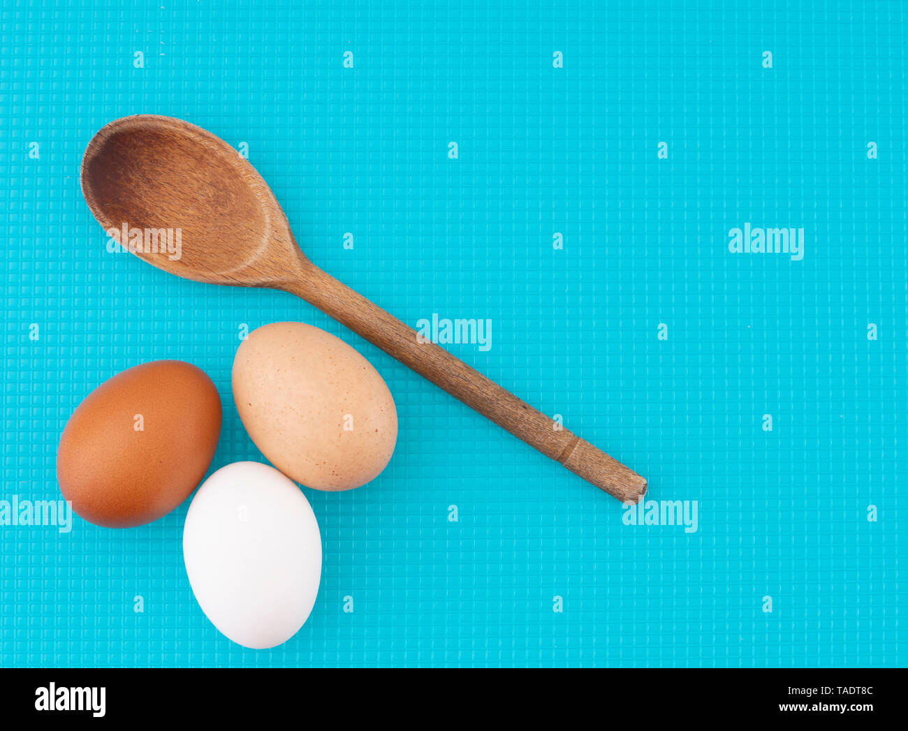 A diversity of eggs. Three chicken, hens eggs on turquoise kitchen board. Different colors: brown white and speckled. Stock Photo