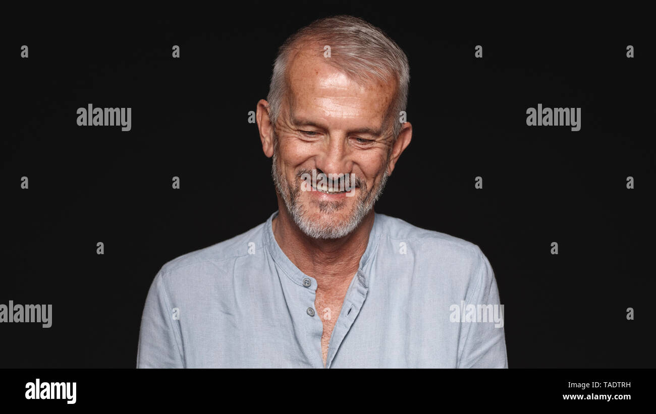 Close up of a laughing senior man against black background. Portrait of smiling senior man looking down. Stock Photo