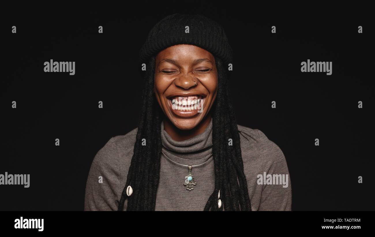 Portrait of african female having long dreadlocks laughing with eyes closed. Laughing woman isolated on black background. Stock Photo
