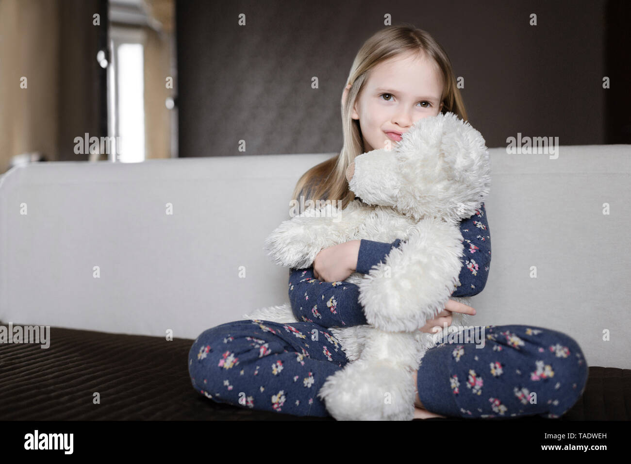 Portrait of smiling little girl wearing pyjama with floral design holding white teddy bear Stock Photo