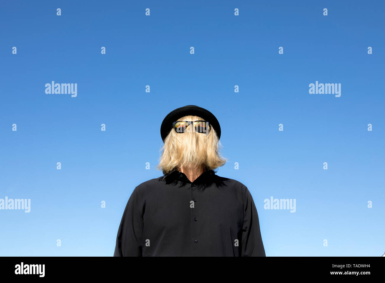 Blond hair covering man's face wearing sunglasses and bowler hat Stock Photo