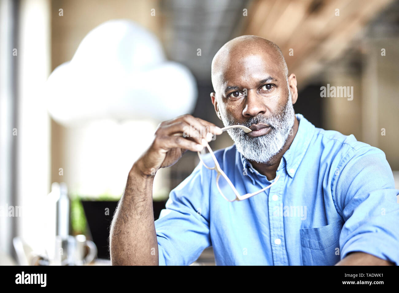 Mature businessman in office thinking with cloud balloon in background Stock Photo