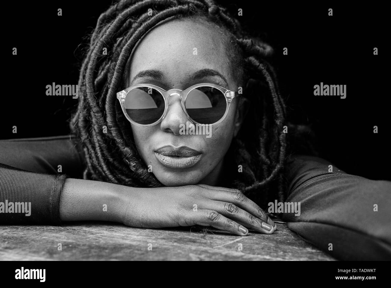 Portrait of woman with dreadlocks wearing sunglasses in front of black background Stock Photo