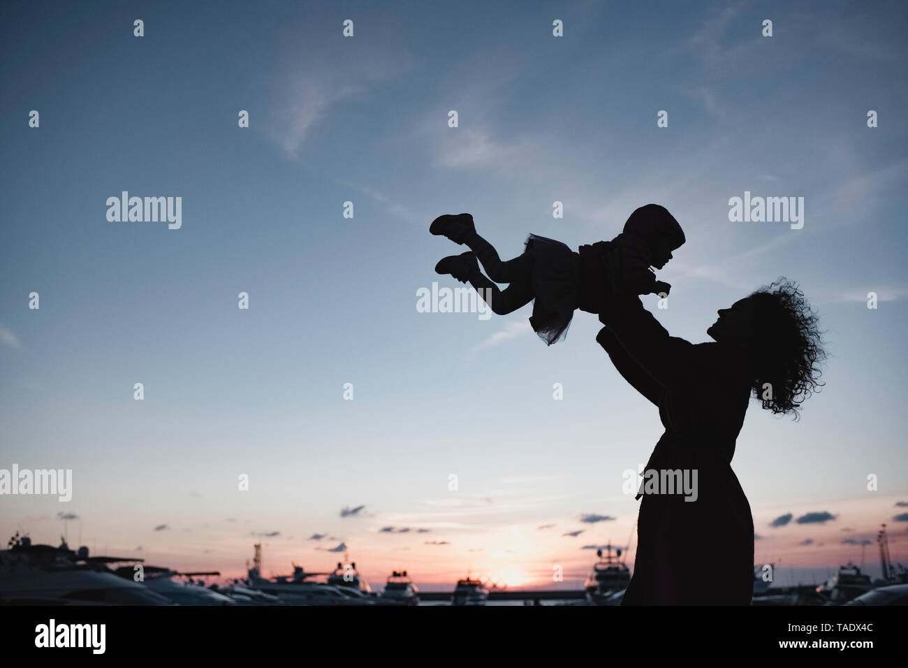 Silhouette of mother playing with her daughter at sunset Stock Photo