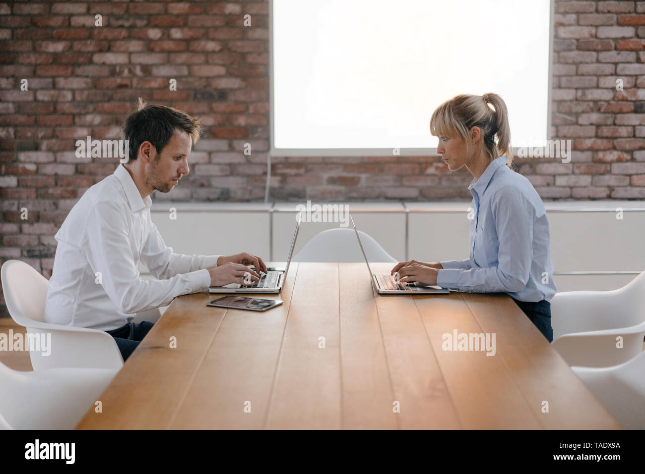 Businessman and woman sitting at desk, working on laptop Stock Photo