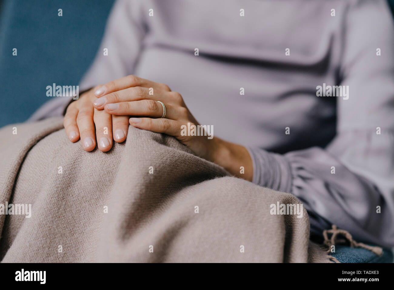 Folded hands of a woman on a blanket over her knees Stock Photo