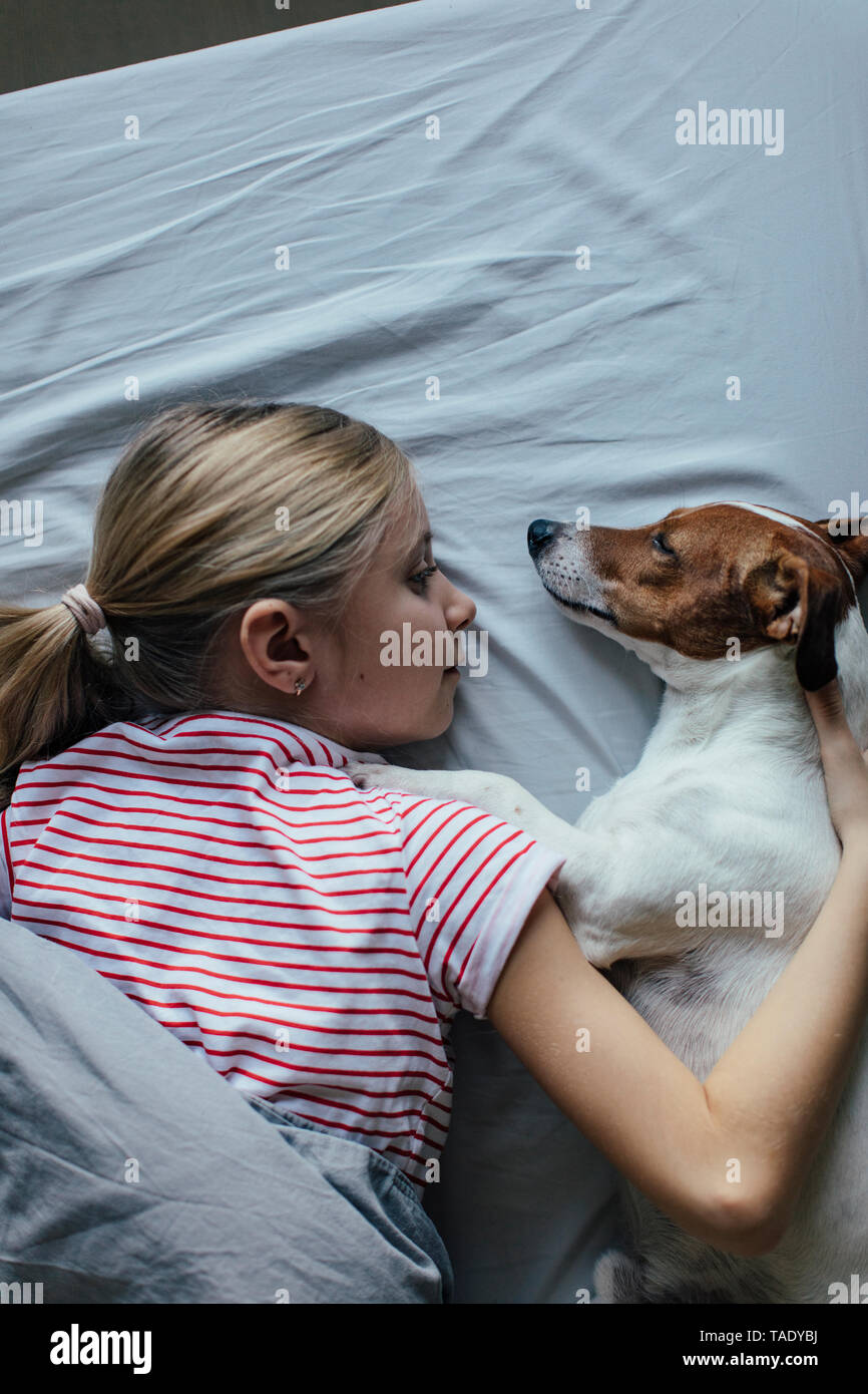 Blond girl lying on bed cuddling with her dog Stock Photo
