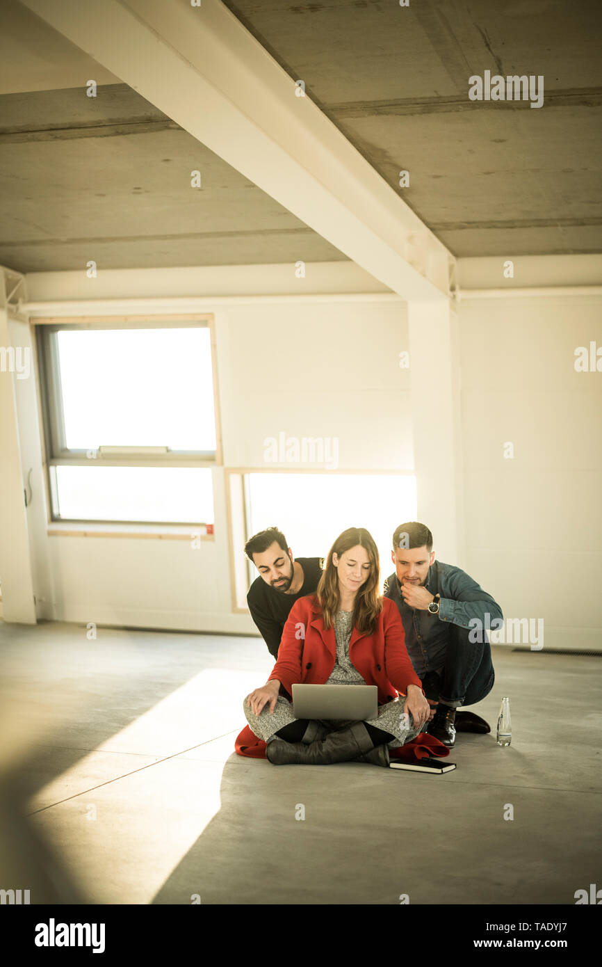 Colleagues sitting on floor of empty office rooms, making plans, using laptop Stock Photo