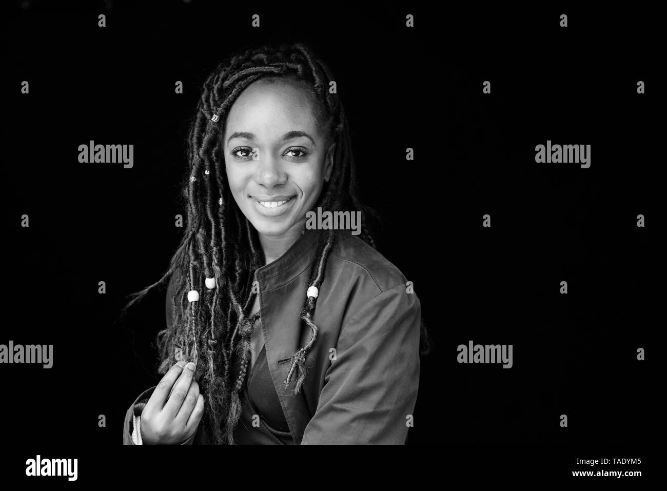 Portrait of smiling woman with dreadlocks in front of black background Stock Photo