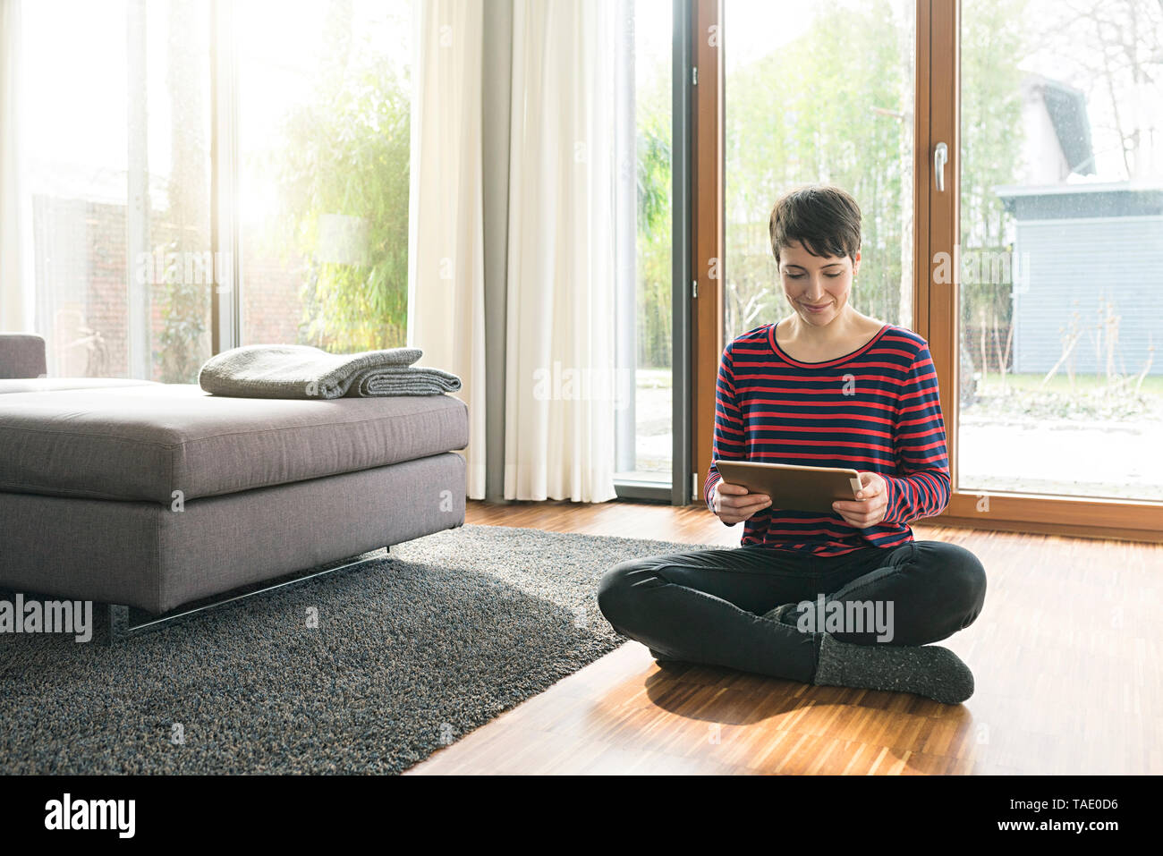 Portrait of woman sitting on the floor of living room using digital tablet Stock Photo