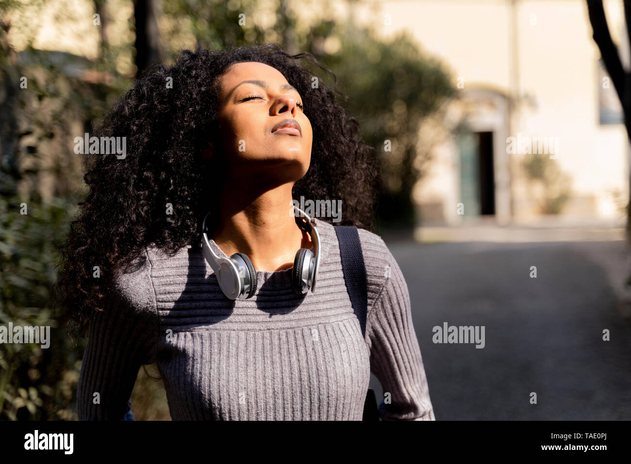 Portrait of a woman with headphones, enjoying the sun with closed eyes Stock Photo