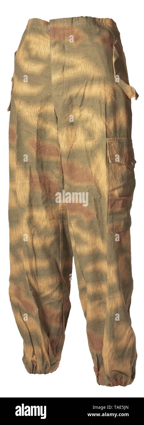 A pair of camouflage trousers for Panzer and assault gun crews in similar cut to the drill cloth trousers of the special clothing issue One side with material imprinted in marsh pattern camouflage with sheet metal buttons. Raised rear, an incorporated strap at the waist and covered fly. The oblique front pockets, both integrated hip pockets and left-sided upper leg pocket with curved flaps closable by a single button. Leg terminals with elastic bands, pocket sacks and reinforcements of base cloth. historic, historical, army, armies, armed forces, military, militaria, object, Editorial-Use-Only Stock Photo