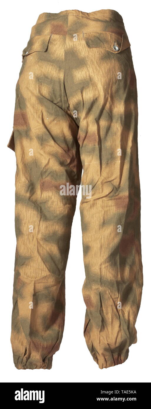 A pair of camouflage trousers for Panzer and assault gun crews in similar cut to the drill cloth trousers of the special clothing issue One side with material imprinted in marsh pattern camouflage with sheet metal buttons. Raised rear, an incorporated strap at the waist and covered fly. The oblique front pockets, both integrated hip pockets and left-sided upper leg pocket with curved flaps closable by a single button. Leg terminals with elastic bands, pocket sacks and reinforcements of base cloth. historic, historical, army, armies, armed forces, military, militaria, object, Editorial-Use-Only Stock Photo