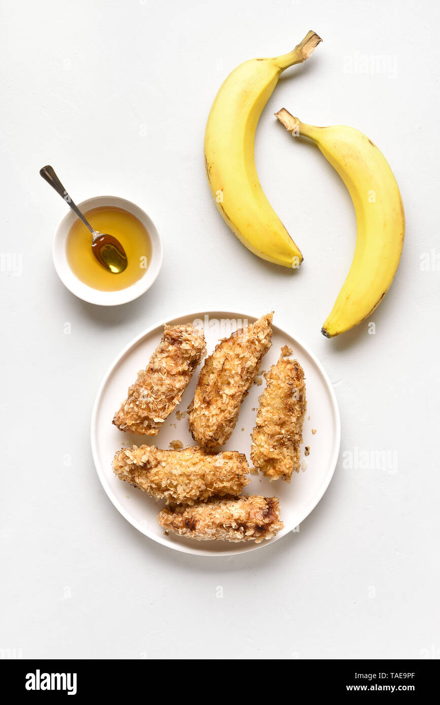 Tasty deep fried bananas on plate over white stone background. Dessert