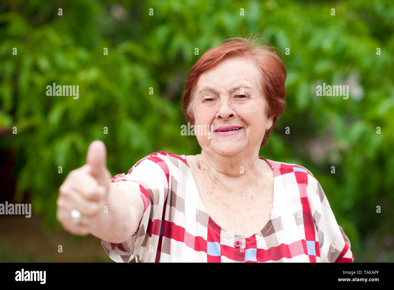 Elderly woman with thumb up laughing outdoors. Senior. Looking at camera. 70s. Stock Photo