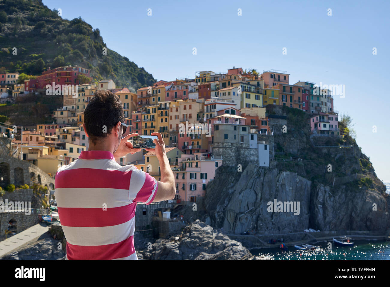 Italy, Liguria, La Spezia, Cinque Terre National Park, man using smartphone, photographing Manarola Stock Photo