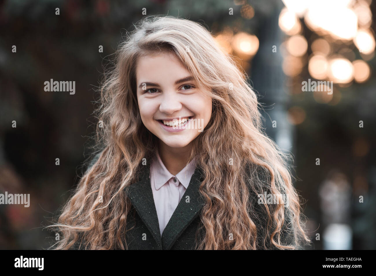 Smiling blonde teen girl 14-16 year old with curly hair wearing winter  jacket over sunset at background. Looking at camera Stock Photo - Alamy